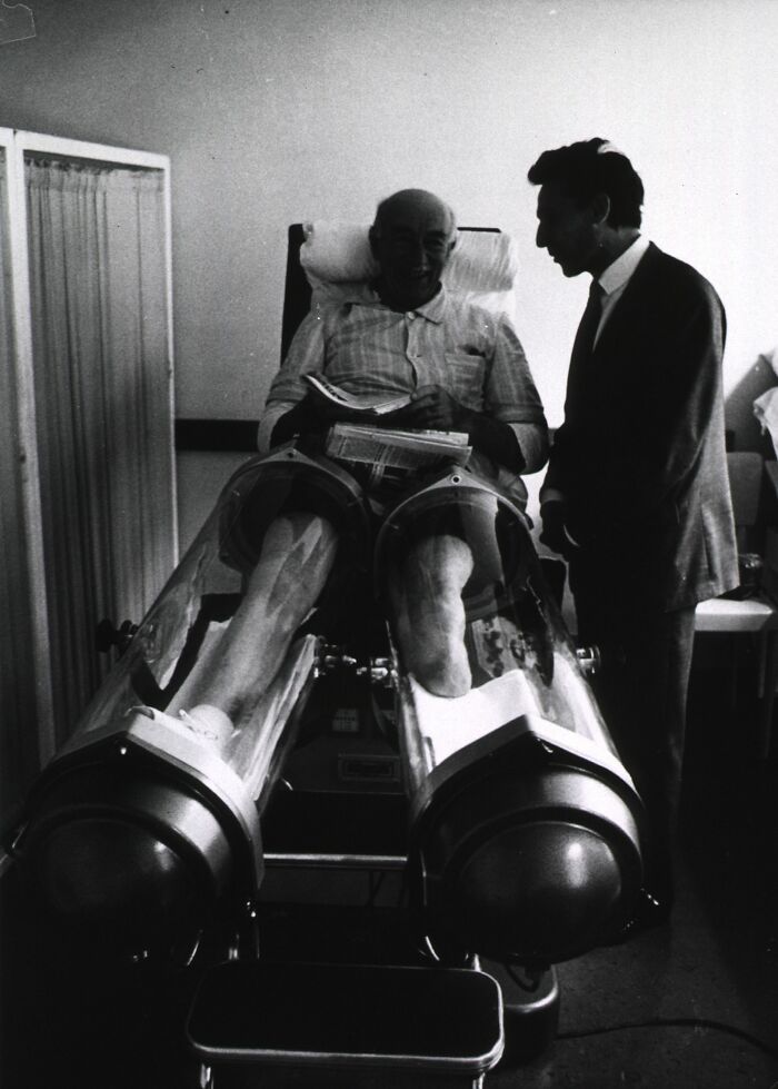Vintage medical device showing a patient using leg hydrotherapy tanks in a historic healthcare treatment setting.