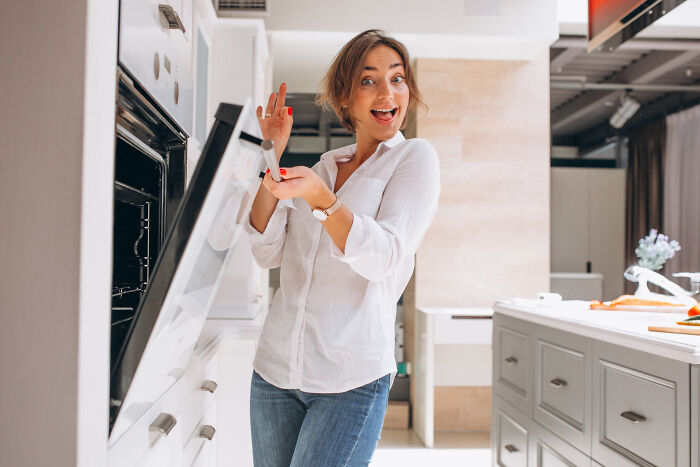Woman in casual clothes opening an oven in a modern kitchen, illustrating childhood norms that seem weird.