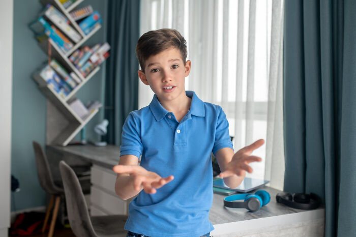 Young boy in a blue shirt gestures in a room, illustrating childhood norms that people later found extremely weird.