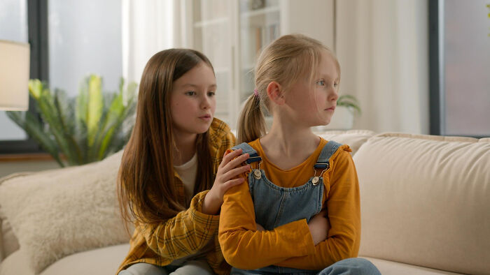 Two young girls sitting on a couch, one comforting the other, highlighting childhood norms and behaviors.
