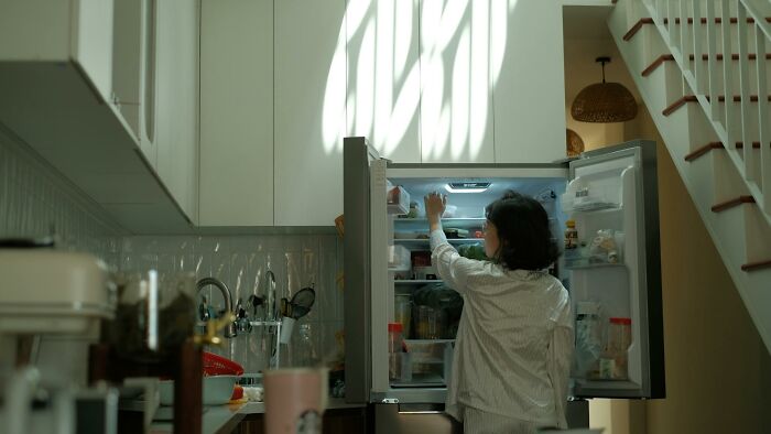 Person reaching into a refrigerator in a kitchen, illustrating childhood norms that seem weird in hindsight.
