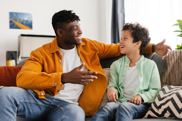 Man and child smiling and talking on a couch, illustrating childhood norms that people grew up to realize were weird.