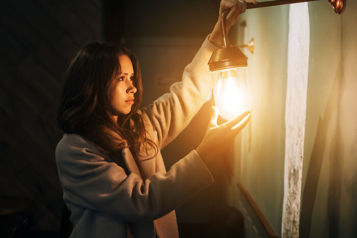 Young woman adjusting a glowing lantern indoors, illustrating childhood norms that people grew up to realize were weird.