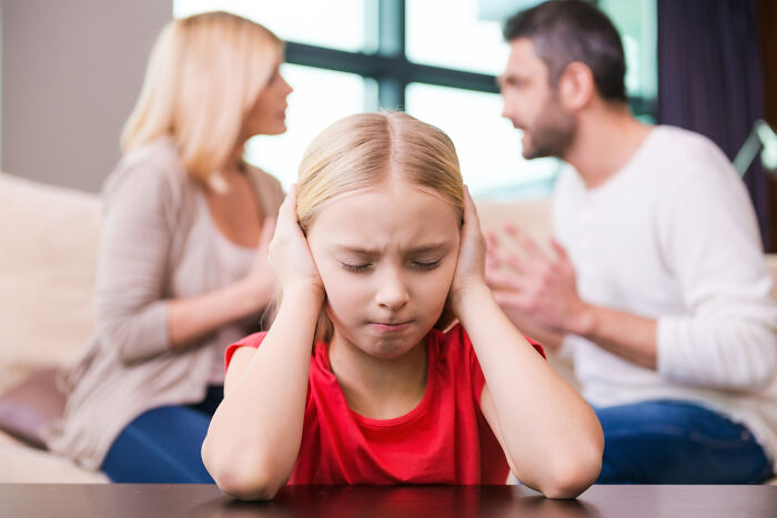 Child covering ears while parents argue in the background illustrating childhood norms that seem weird as adults.