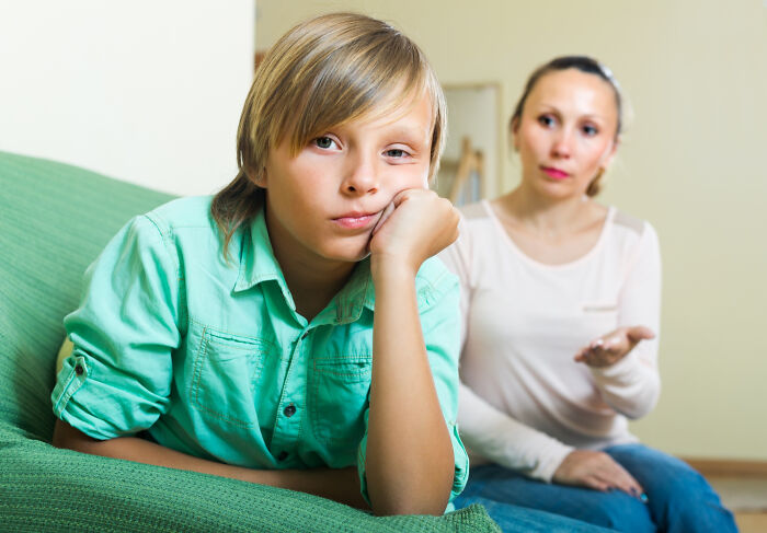 A bored child in a green shirt ignoring a woman explaining childhood norms that later seemed weird.