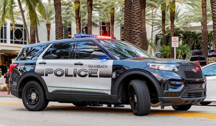 Miami Beach police car with flashing lights parked on a street lined with palm trees, highlighting childhood norms awareness.