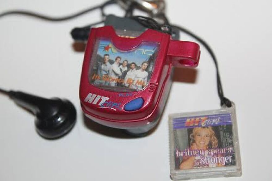 A red HitClips player with earbuds, featuring *NSYNC on display and a Britney Spears cartridge. Take a trip down memory lane!