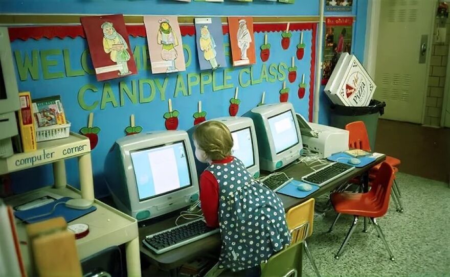 A young child in a classroom computer corner, surrounded by old CRT monitors. A trip down memory lane.