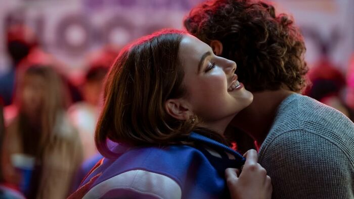 A happy woman in a blue jacket hugging a man from behind at a party, embodying the steamy new romance genre.