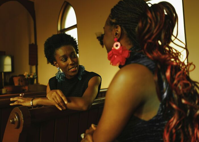 Two women engaged in conversation in a warm-lit room, reflecting on past experiences with kids and bullies.