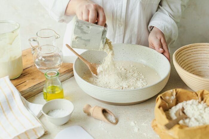Person pouring flour into a bowl while preparing a family baking recipe with traditional ingredients on the table