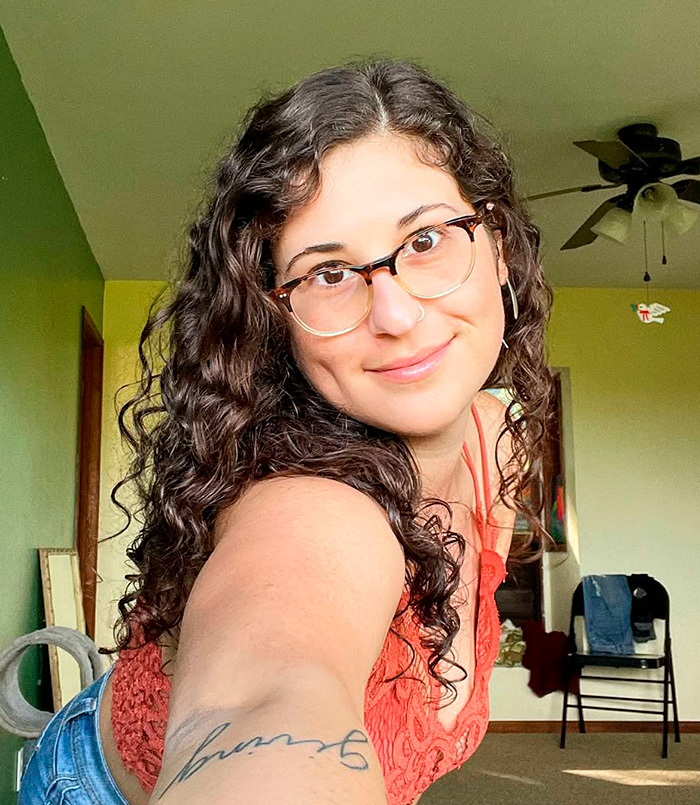 Young woman with curly hair and glasses taking a selfie indoors, related to OpenAI CEO Sam Altman lawsuit news.