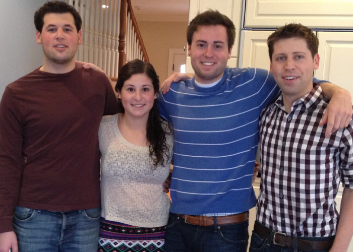 Four young adults standing indoors, casually posed with arms around each other, highlighting OpenAI CEO Sam Altman.