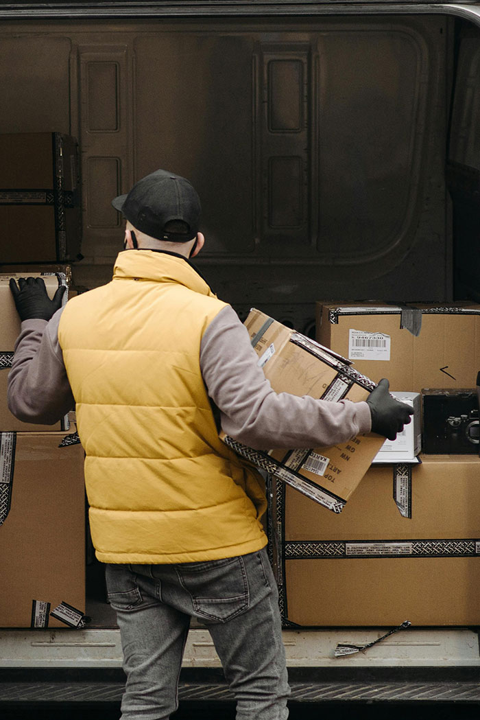 Man in a yellow vest helping an overworked and underpaid friend by carrying multiple delivery boxes in a van.