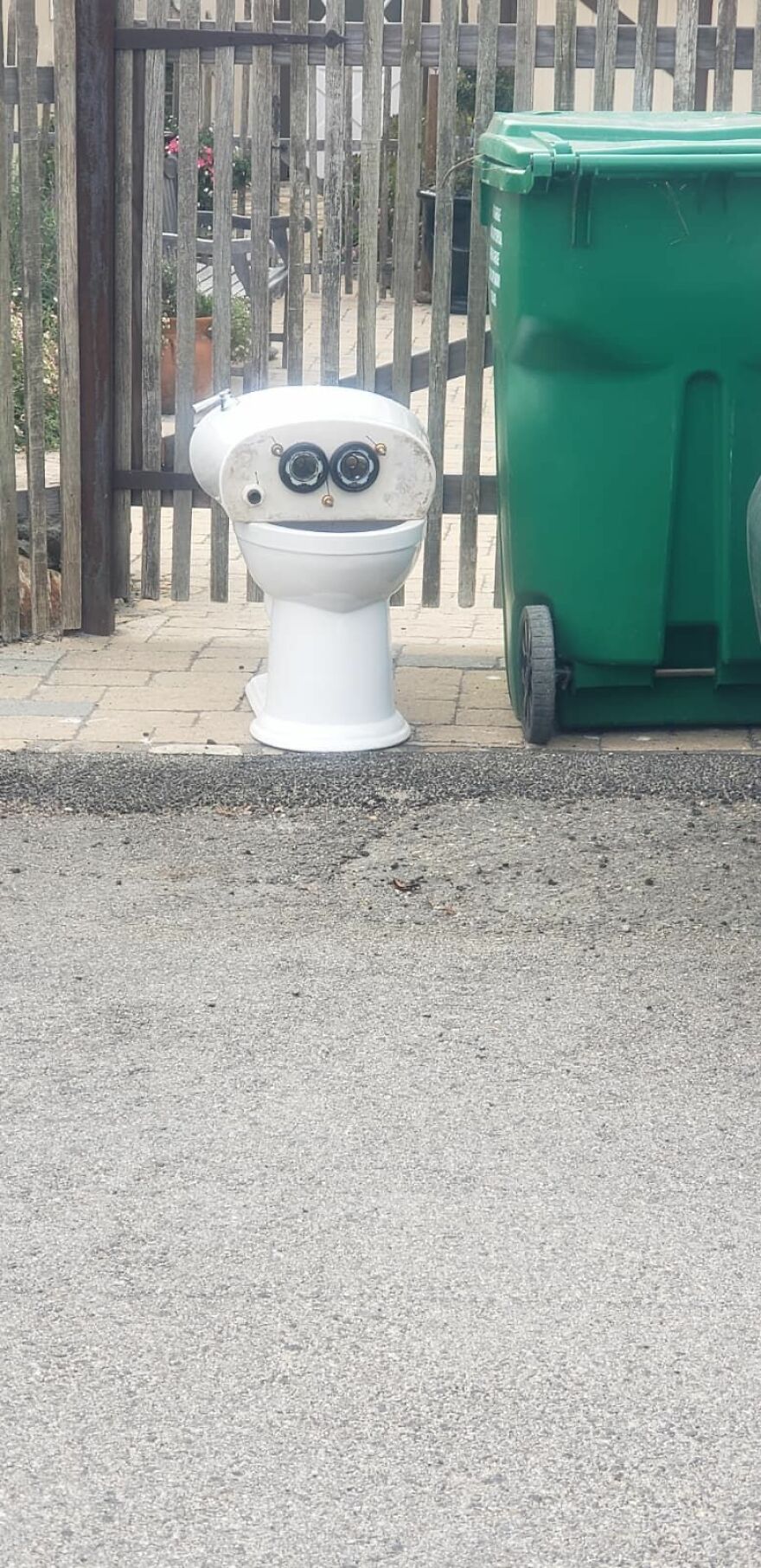Toilet and green trash bin side by side creating pareidolia effect resembling a surprised face outdoors