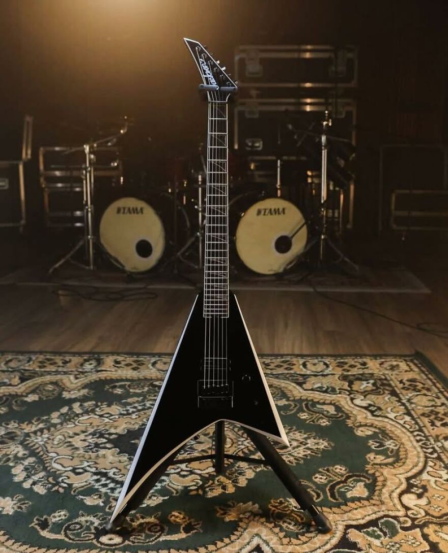 Black electric guitar appearing like a face with drum set eyes in the background, showcasing pareidolia in music gear.