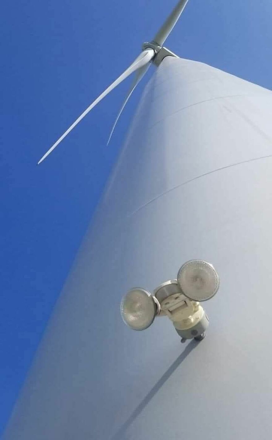 Wind turbine with lights resembling a face, an example of pareidolia against a clear blue sky.