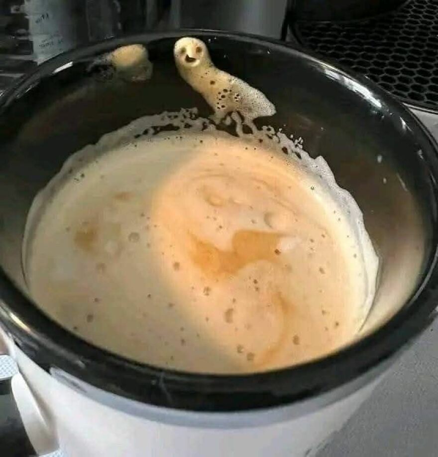 Cup of coffee foam with pareidolia showing a bird shape formed by bubbles on the cup edge and foam patterns inside.