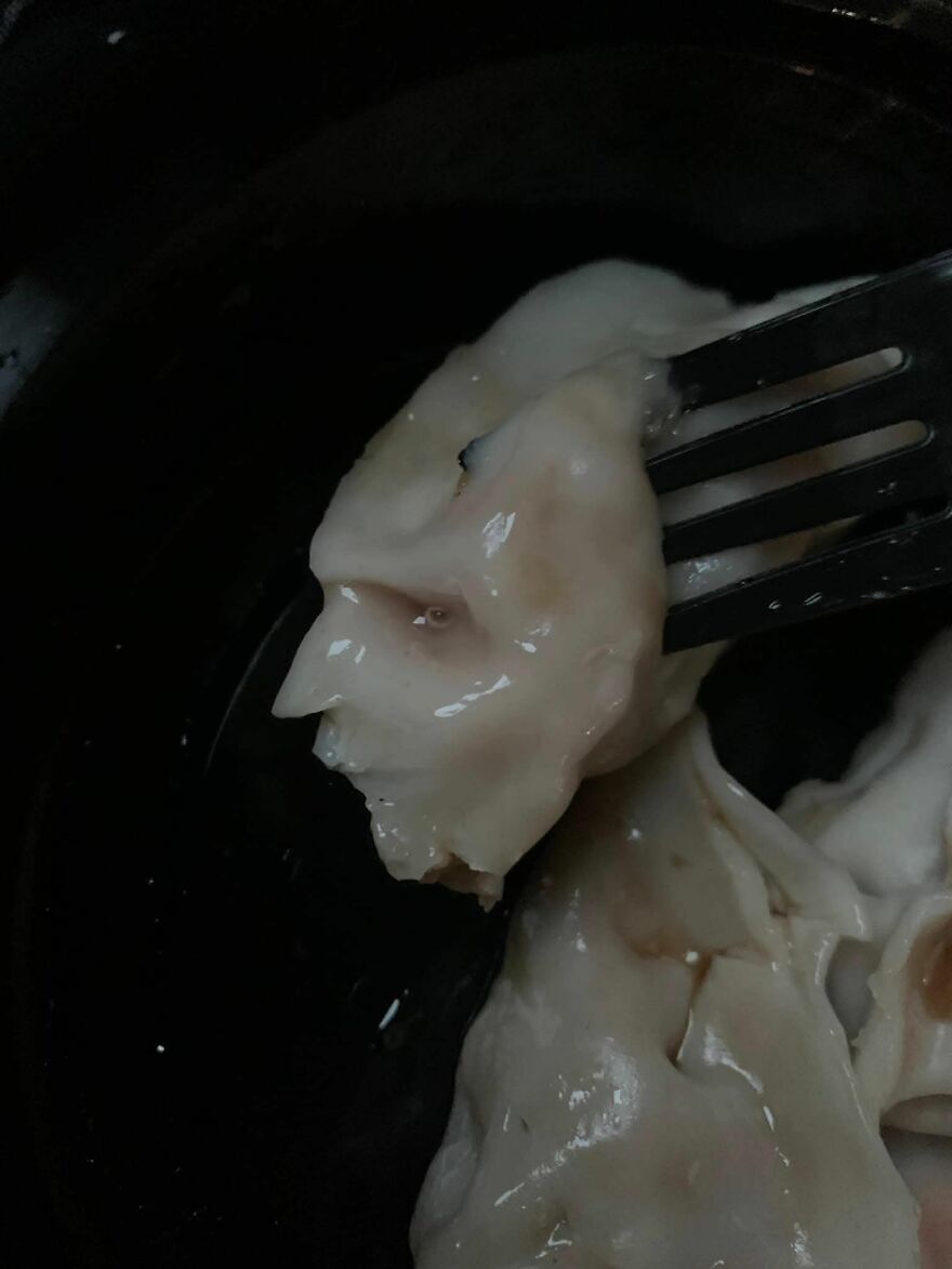 Fork holding dumpling resembling a human face, an example of pareidolia captured in a close-up food photo.