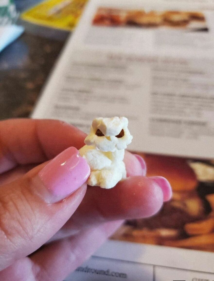 Hand holding a piece of popcorn that looks like an angry owl face, an example of pareidolia in everyday objects.