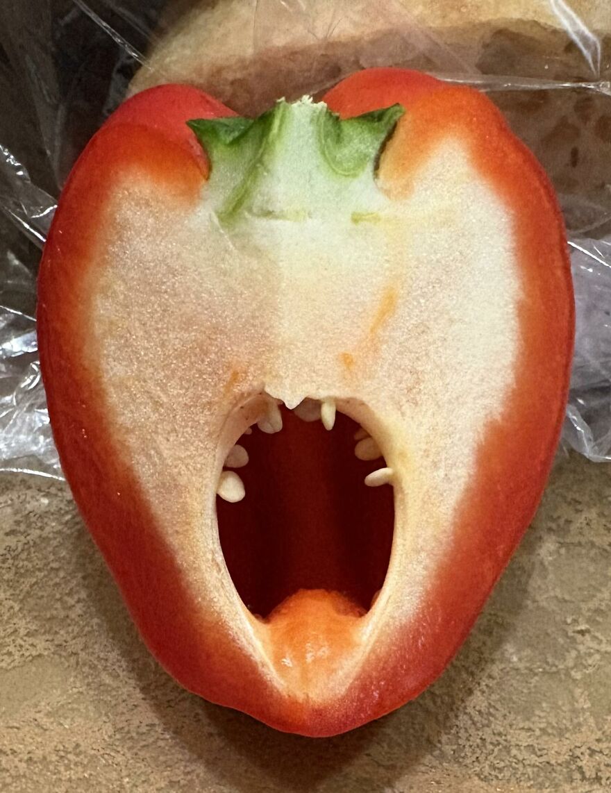 Red pepper sliced open showing seeds that resemble teeth, creating a pareidolia effect like a screaming face.