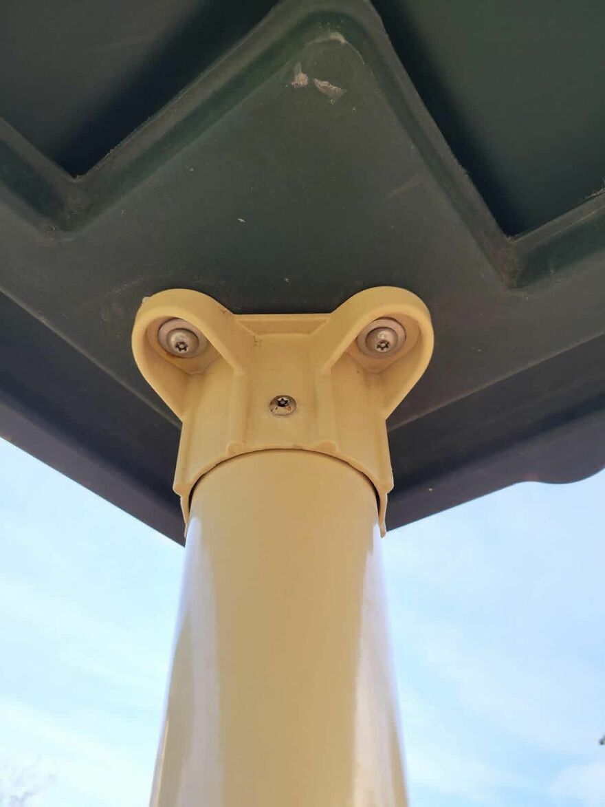 Yellow metal pole with screws resembling a face, an example of pareidolia seen in everyday objects outdoors.