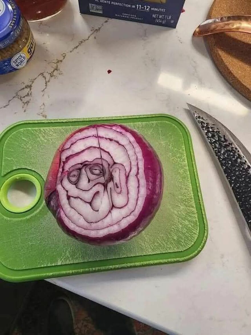 Red onion sliced on a green cutting board showing a face-like pattern, an example of pareidolia captured in a kitchen.