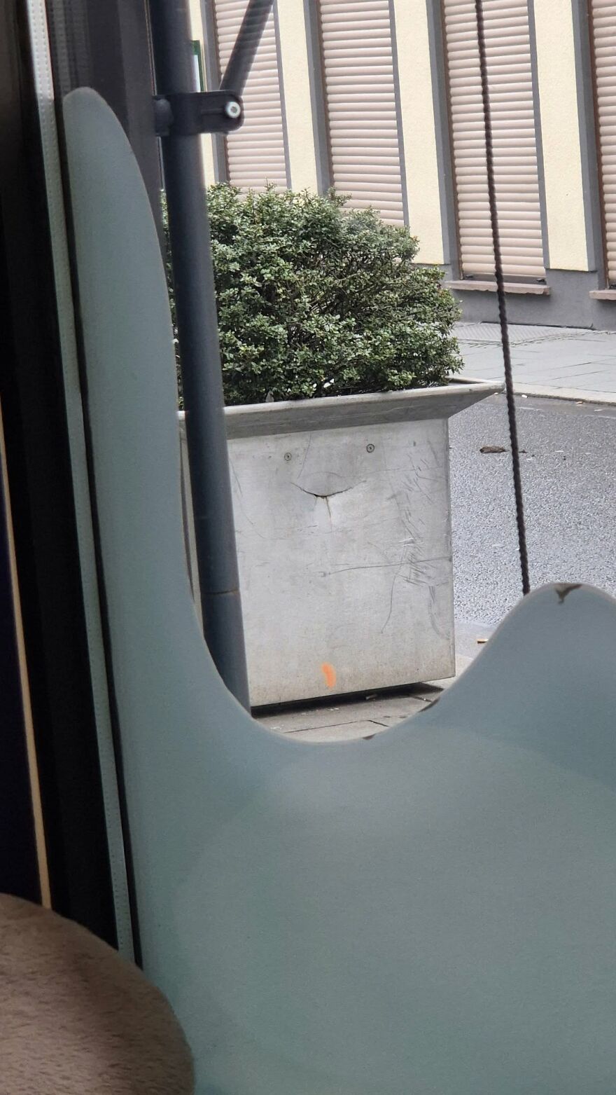 Concrete planter with green bush showing pareidolia face-like pattern on urban street background.