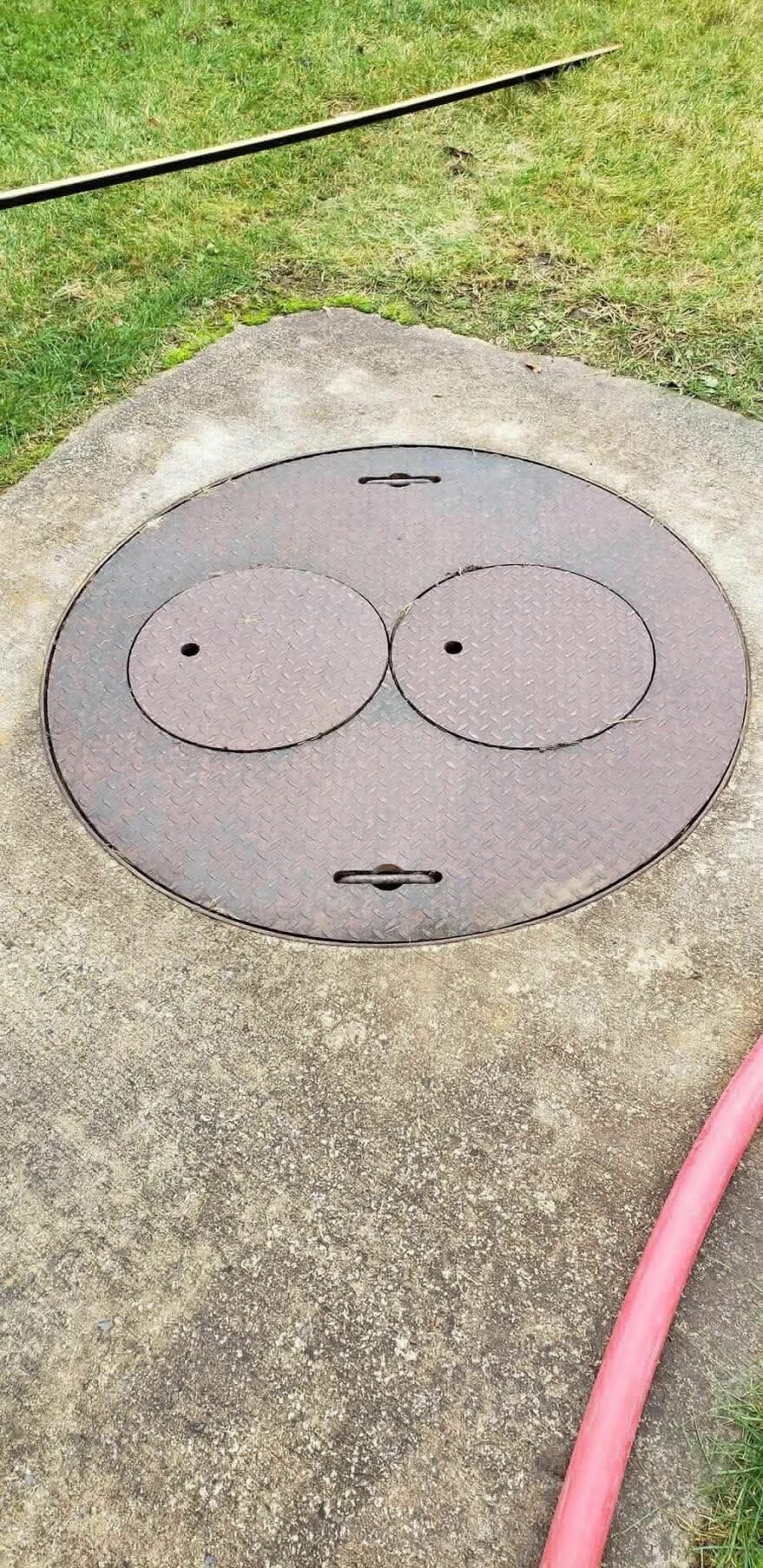 Round metal manhole cover on concrete resembling a surprised face, an example of pareidolia in everyday objects.