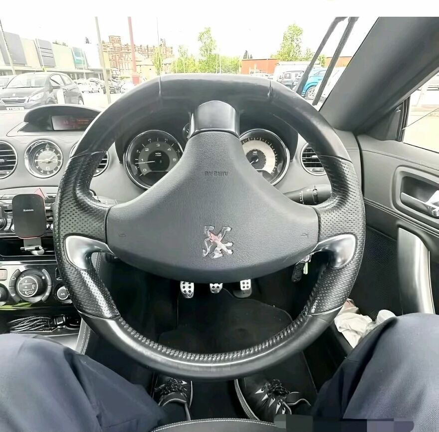 View of a car interior focusing on the steering wheel, pedals, and dashboard demonstrating pareidolia in everyday objects.