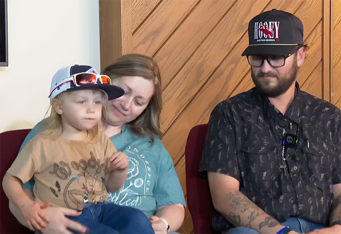 Woman and child with family member sitting indoors, related to police fatally taking down woman attacking toddler at Walmart.