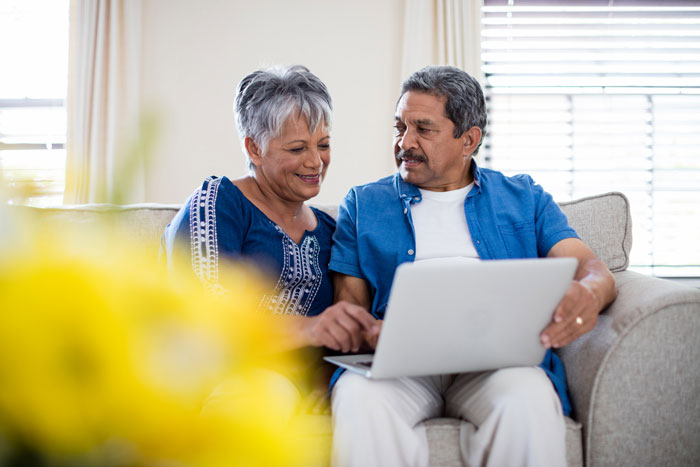 Older couple sitting on couch using laptop together, reflecting on parenting and their son's independence at 18 years old.