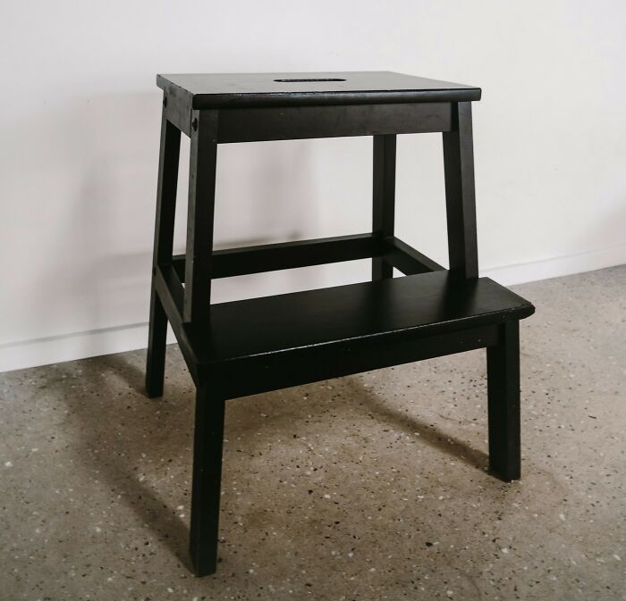 Black wooden step stool on a speckled floor against a white wall illustrating practical parents tips and tricks.
