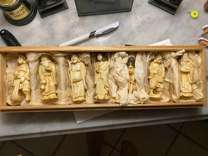 A wooden box holds several carved ivory-colored figurines, individually wrapped, representing the unusual possessions people seek to understand.