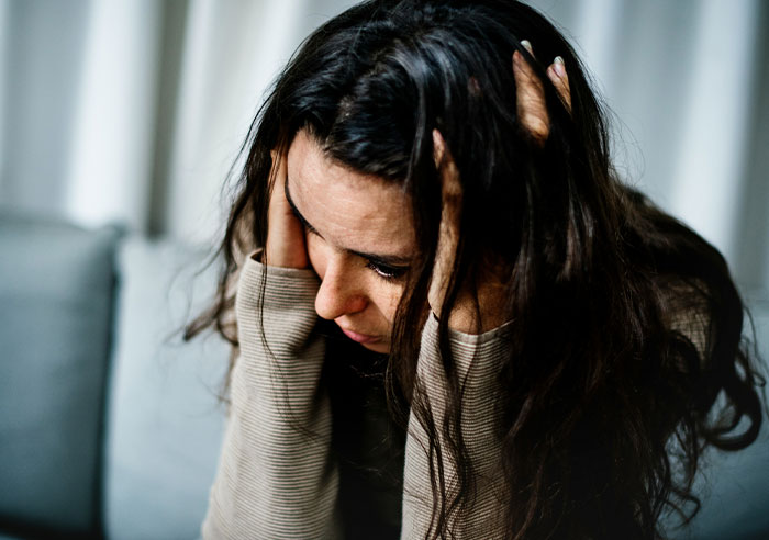 A woman with dark hair, looking stressed with hands on her head, contemplating needing better friends.