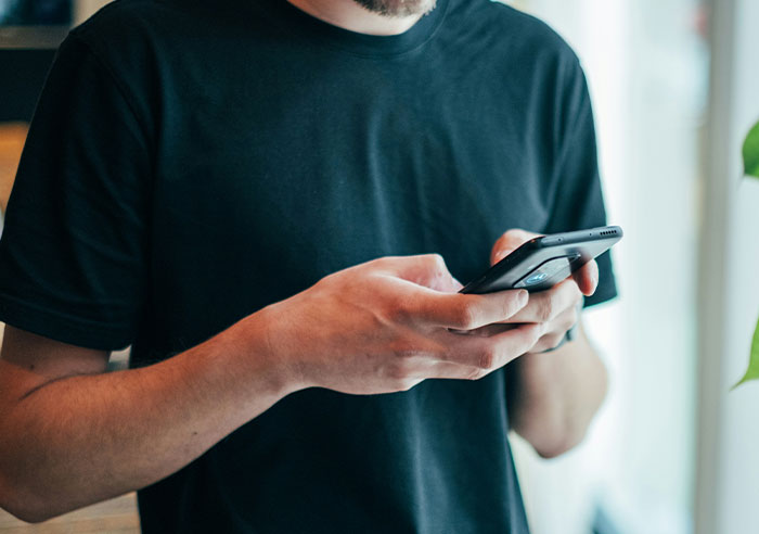 A man in a black t-shirt uses his smartphone. He realized he needed better friends and is checking his Epstein files.