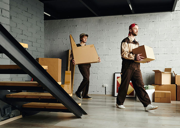 Two movers carrying boxes in a room filled with cardboard boxes, reflecting on the importance of better friends.