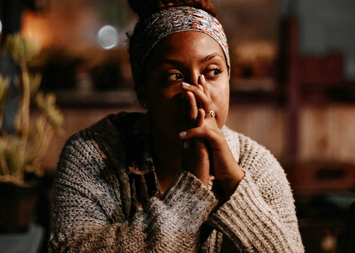 A woman with a patterned headband and knitted sweater, hands clasped, looking reflective. She might need better friends.