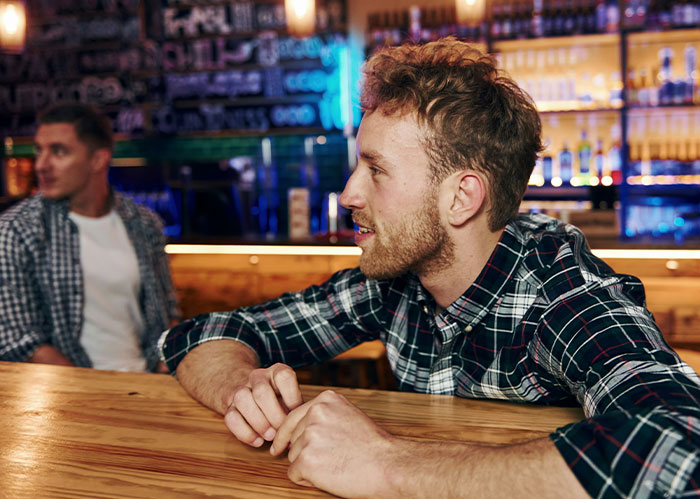 Two men in plaid shirts at a bar. One man talks while the other listens, pondering if they need better friends.