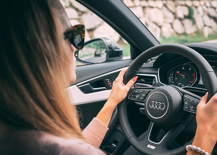 Woman with sunglasses driving an Audi, hands on the steering wheel, on the road. Do you need better friends?