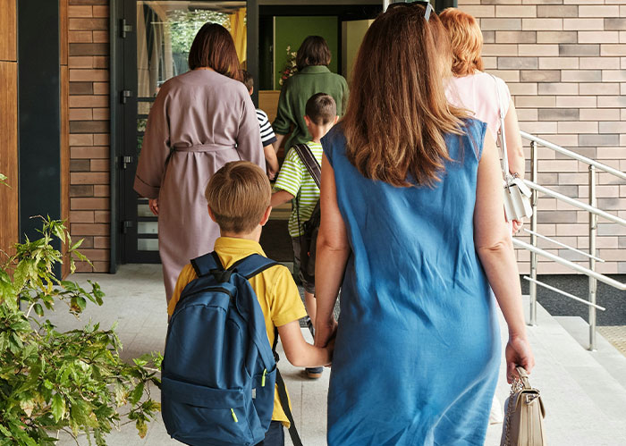 A woman in a blue dress holding a boy's hand, entering a building with other adults and children. The importance of having better friends.