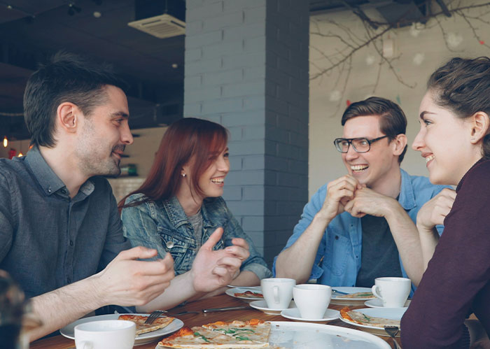 Four friends enjoying pizza and coffee, laughing together, showcasing good friends.