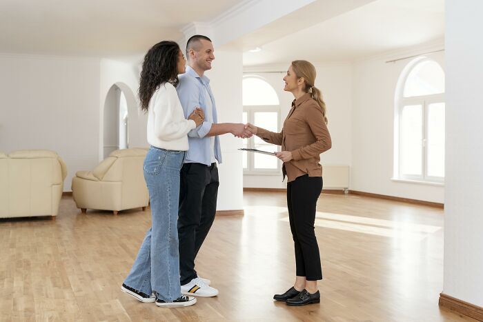 A happy couple shaking hands with a realtor in an empty room, possibly discussing petty revenge stories.