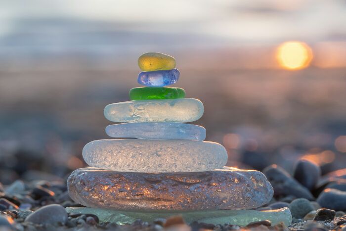 Stack of colorful sea glass stones balanced on a beach at sunset, illustrating normal family activities now seen as bizarre.
