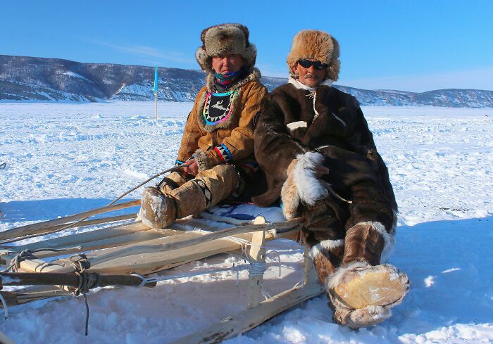 Two people in traditional fur clothing sitting on a wooden sled in snowy landscape, illustrating random facts about bodies.