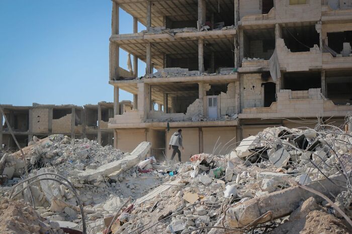Person walking through rubble near a partially destroyed building, illustrating stories about moms in challenging situations.