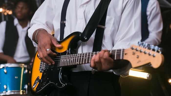 Musician playing electric guitar in a band setting, highlighting iconic 80s and 90s music performers style and vibe.
