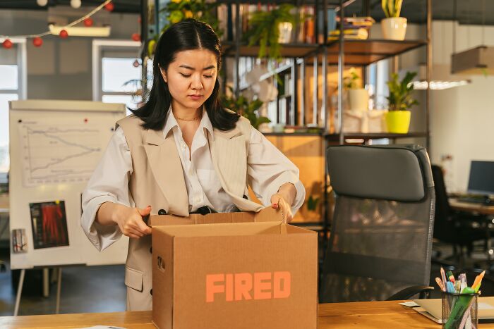 A woman with dark hair in a beige vest packing a box labeled FIRED. This scene could be one of the disturbing sounds people heard.