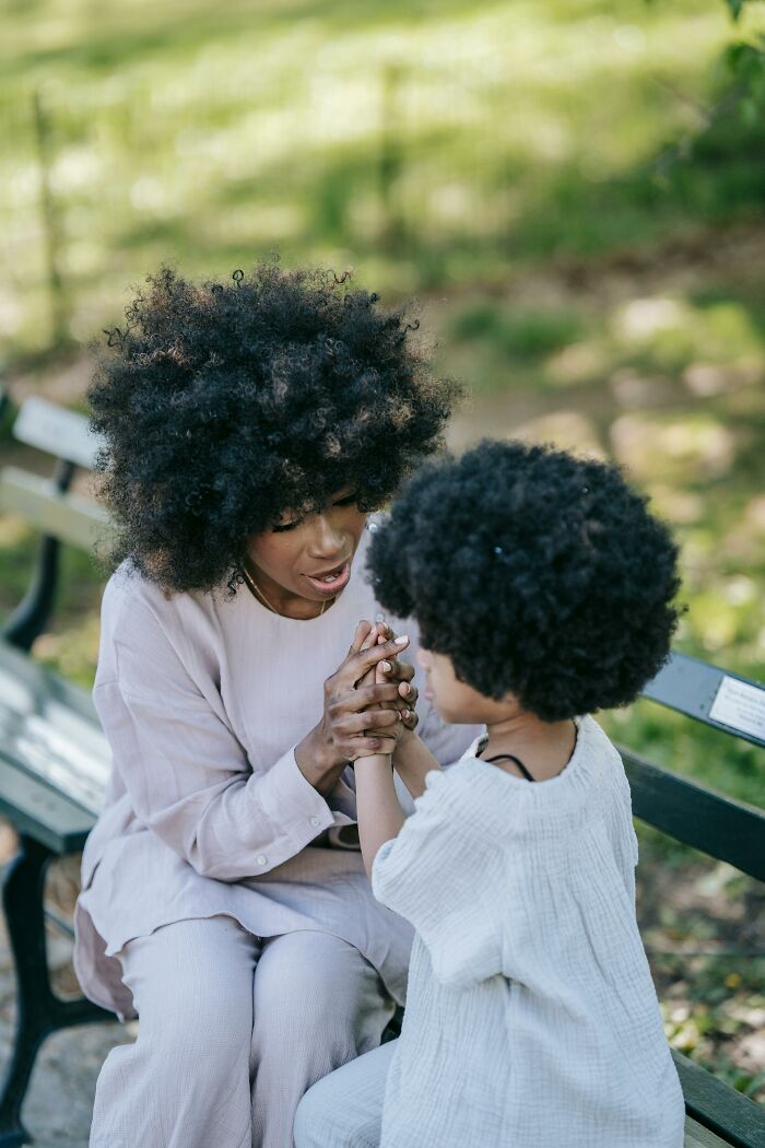 A parent gently holds their child's hands while sharing family secrets on a park bench.