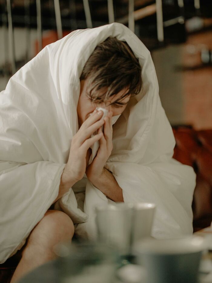 Man wrapped in blanket blowing his nose, illustrating weird and interesting medical facts about health and illness.